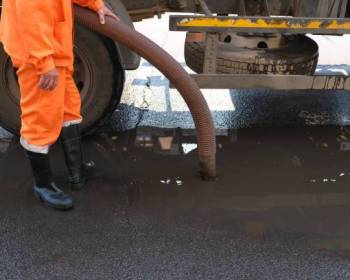 worker pumps out water with a special pump. cleaning of drains on the street. a man in an orange uniform and black rubber boots close-up.