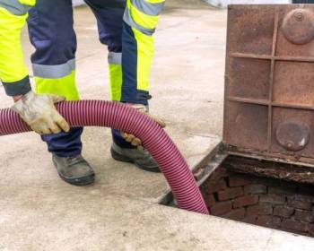 Sewer service worker cleaning, unclogging and draining sewage manhole. Home insurance concept.